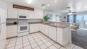 A modern kitchen with white cabinetry, a granite countertop, and a welcome sign.
