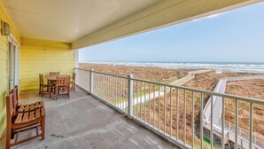 A balcony with a view of the beach and a wooden table and chairs.
