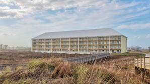 A multi-story hotel with a flat roof, located in a coastal area with a boardwalk leading to it.