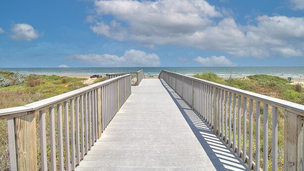 A wooden boardwalk leading to the beach with a clear view of the ocean and sky.