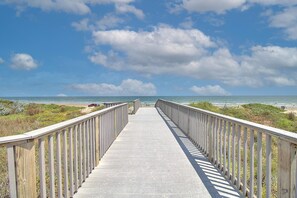 Une promenade en bois menant à la plage, offrant une vue dégagée sur l’océan et le ciel.