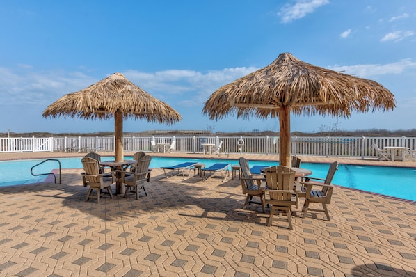 A poolside area with thatched umbrellas, lounge chairs, and a pool.
