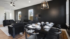 A modern dining area with a dark wall, black furniture, and a geometric pendant light.