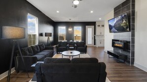 A modern living room with a black and white color scheme, a fireplace, a flat-screen TV, and a ceiling fan.