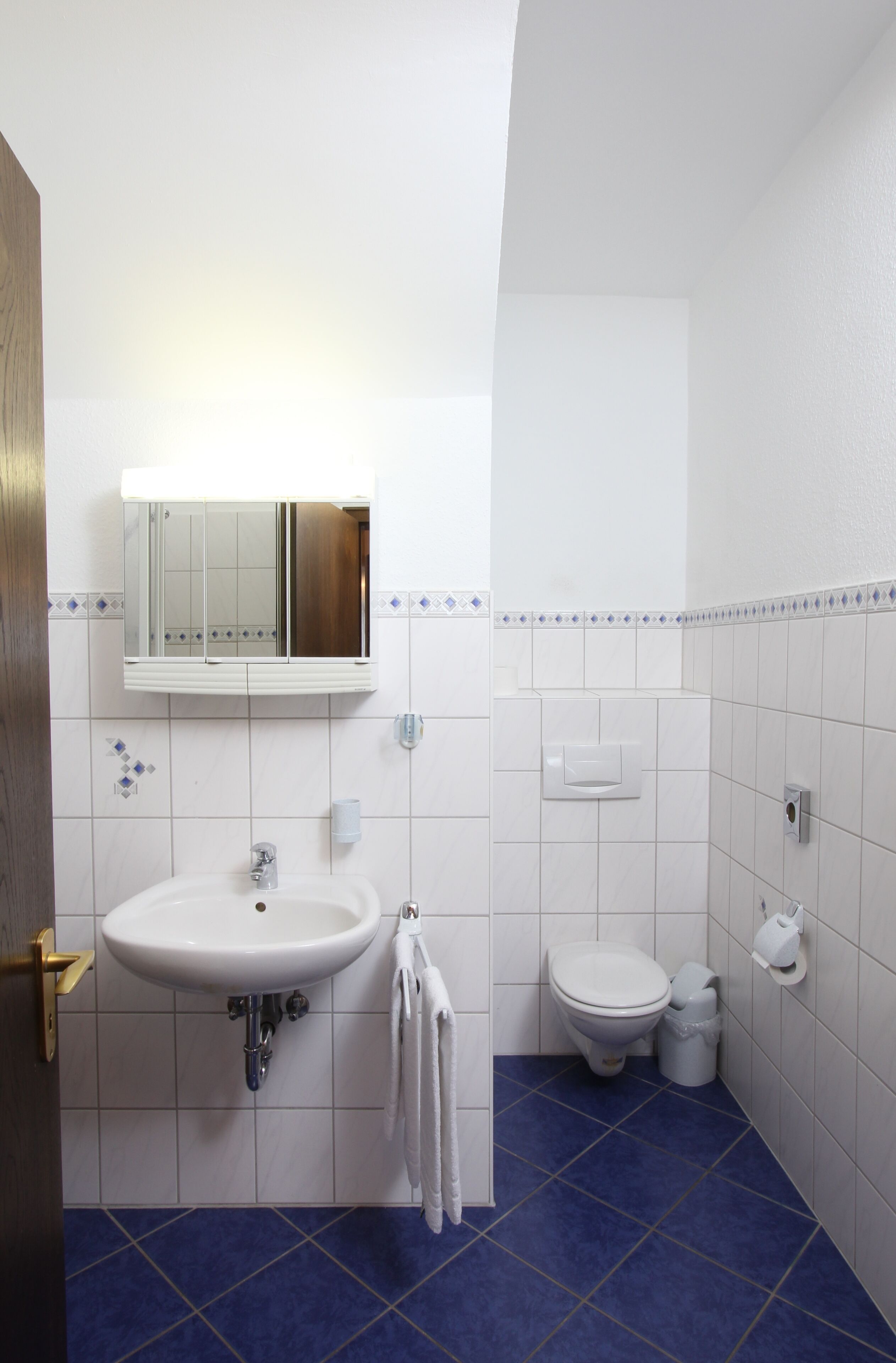 A bathroom with a sink, mirror, toilet, and blue-tiled floor.
