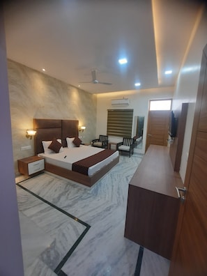 A modern bedroom with a large bed, bedside tables, a ceiling fan, and a TV mounted on the wall. - THE HIGHCLASS HOTEL (Bathinda)