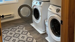 Une buanderie équipée de deux machines à laver et de deux sèche-linge à chargement frontal superposés, d’un tapis à motifs et d’une fenêtre donnant sur la forêt.