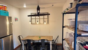 Une cuisine de taille réduite, avec une table en bois, quatre chaises, un réfrigérateur et une étagère contenant de la verrerie.