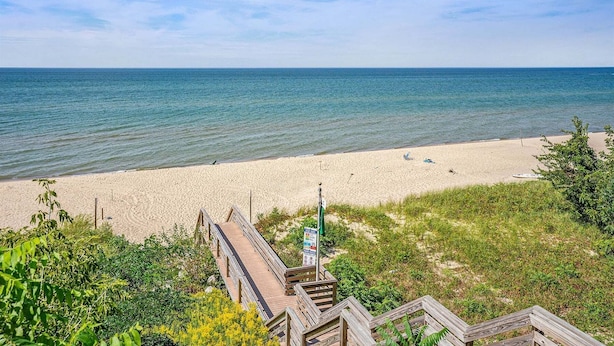 A beach with a wooden boardwalk leading to the shore, clear skies, and calm sea. - Sandy Feet Retreat: Like-New, Harbor Club South Haven, Year-Round Pool & Hot Tub (South Haven)