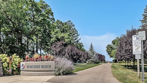 A sign for Newcome Beach with a pathway leading to it, surrounded by trees and a clear sky. - Sandy Feet Retreat: Like-New, Harbor Club South Haven, Year-Round Pool & Hot Tub (South Haven)