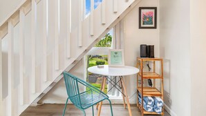 A staircase leading to a balcony with a view of greenery, a white table with a chair, and a wooden shelf with towels.