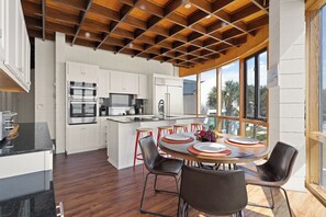 A modern kitchen with white cabinets, stainless steel appliances, and a large island with stools. - The Iconic Round House (St Simons Island)