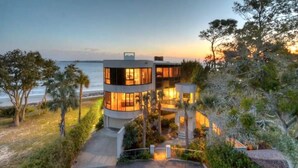 A modern two-story house with a curved design, located near a beach with a view of the ocean. - The Iconic Round House (St Simons Island)