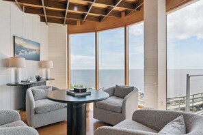 A modern room with a large window overlooking the sea, two armchairs, a round table, and a lamp. - The Iconic Round House (St Simons Island)