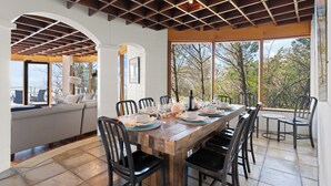 A dining area with a wooden table set for six, surrounded by black chairs, with a view of trees through large windows. - The Iconic Round House (St Simons Island)