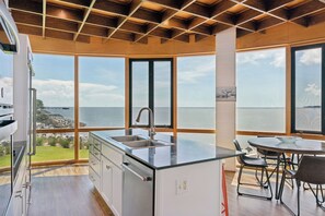 A modern kitchen with a large island, a dining area with a table and chairs, and a view of the sea through large windows. - The Iconic Round House (St Simons Island)