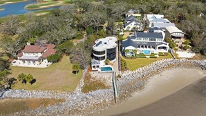 An aerial view of a coastal property with multiple buildings, a swimming pool, and a golf course in the background. - The Iconic Round House (St Simons Island)