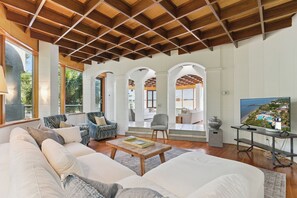 A spacious living area with a high ceiling, large windows, and a view of the outdoors.