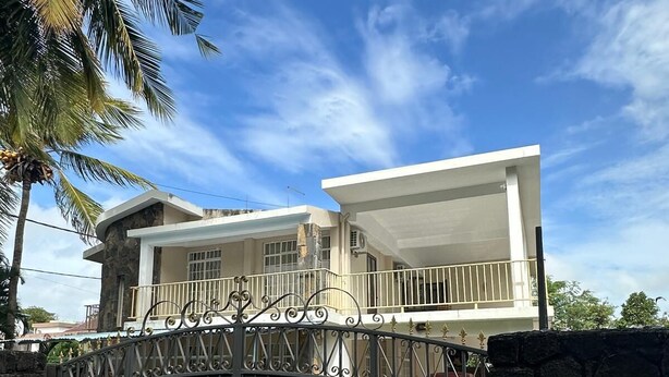 A modern two-story house with a gated entrance, stone walls, and a clear blue sky. - 3-bedroom villa in delightful Calodyne Saint Francois with AC, WiFi (CALODYNE SAINT FRANCOIS)