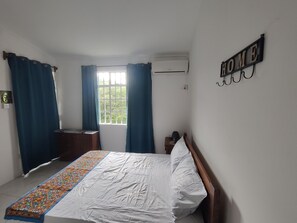 Een slaapkamer met een bed, een raam met gordijnen, een wandairconditioner en een bordje met de tekst 'HOME'.
