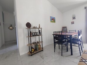 Een eethoek met een tafel en stoelen, een plank met decoratieve objecten, en een deur met een ruitvormige spiegel.
