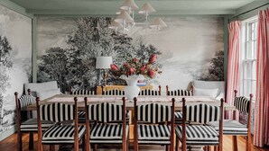 A dining area with a long table, striped chairs, a vase with flowers, and a wall mural. - Beautiful Historic Home | Heated Pool & Hot Tub (Nantucket)