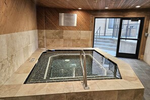 A hot tub with a metal grid floor, surrounded by beige tiles and wooden walls.