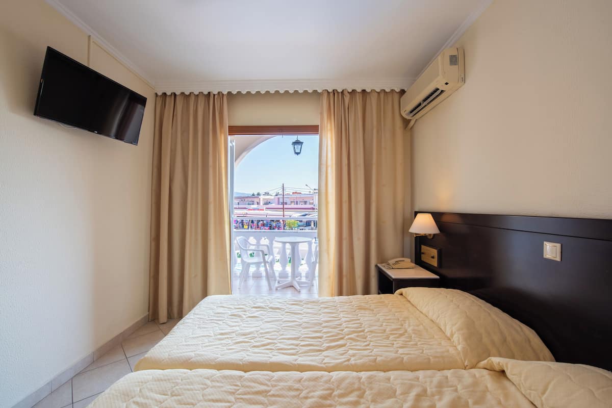 A hotel room with a bed, a TV mounted on the wall, an air conditioning unit, and a balcony with a view of the outside.