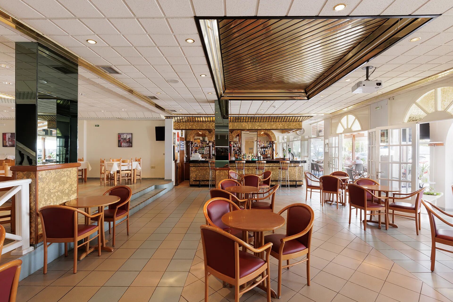 A spacious indoor area with multiple seating arrangements, a bar area, and large windows allowing natural light.