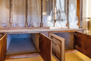 Ein Zimmer mit einem Bettgestell aus Holz, einem großen Fenster mit durchsichtigen Vorhängen und Holzdielen.