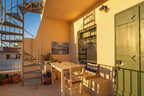 Ein Balkon mit Tisch, Stühlen, Topfpflanzen, einem Gemälde und einer grünen Tür.