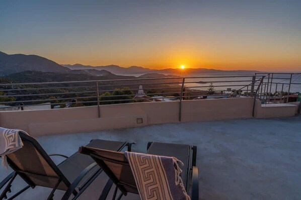 Eine Dachterrasse mit Liegestühlen und Blick auf den Sonnenuntergang über den Bergen.