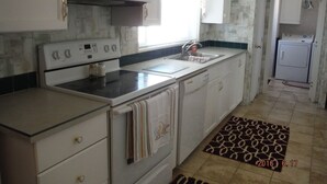 A kitchen with a microwave, stove, sink, and a small laundry area.