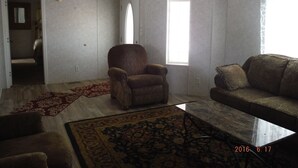 A living room with a ceiling fan, a large window, a door, and a patterned rug.