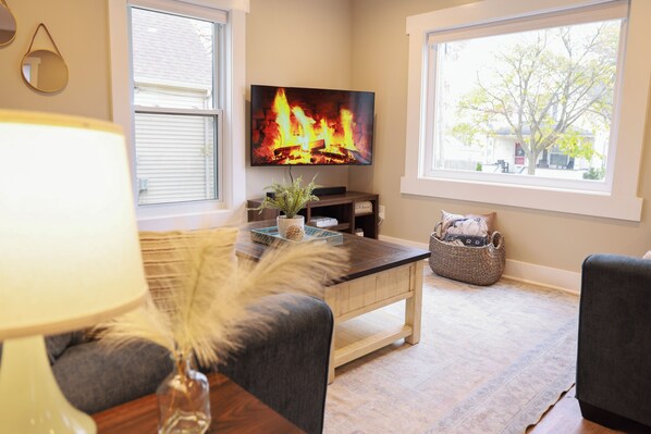 A living room with a TV, a coffee table, and a window with a view of a tree.