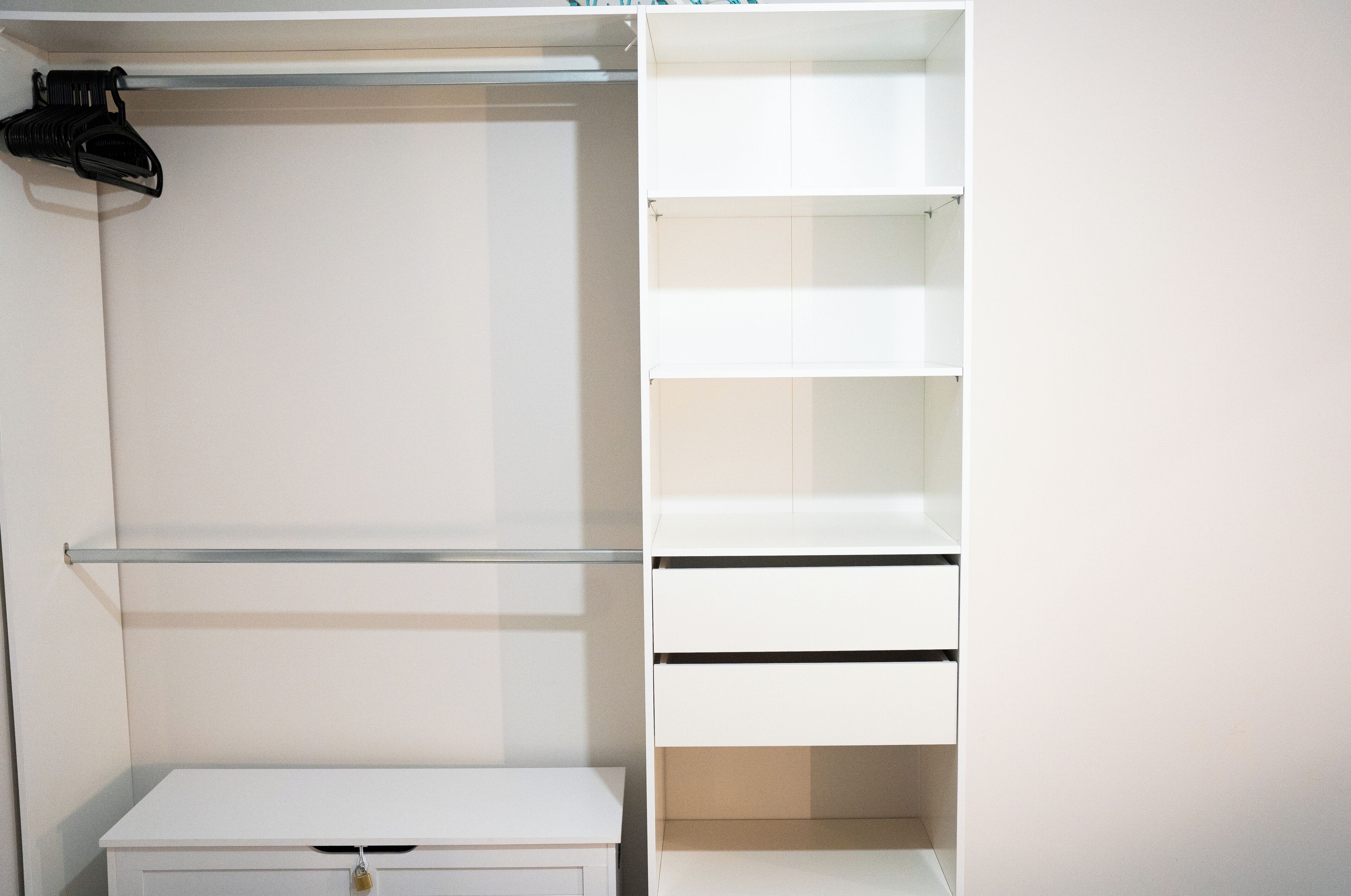 A white closet with open shelves and drawers, a hanging rod, and a small table.