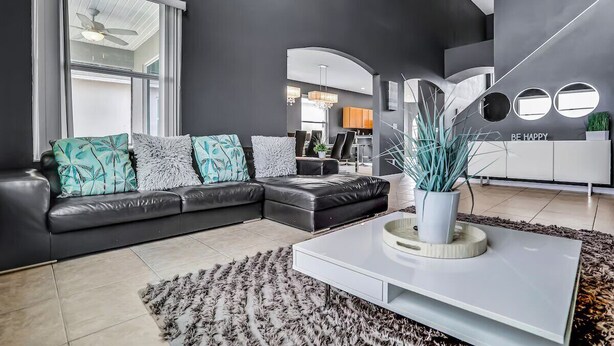 A modern living room with a black leather sofa, a white coffee table, and a large window.