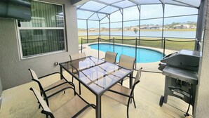 A covered patio with a glass table and chairs, a grill, and a view of a lake.