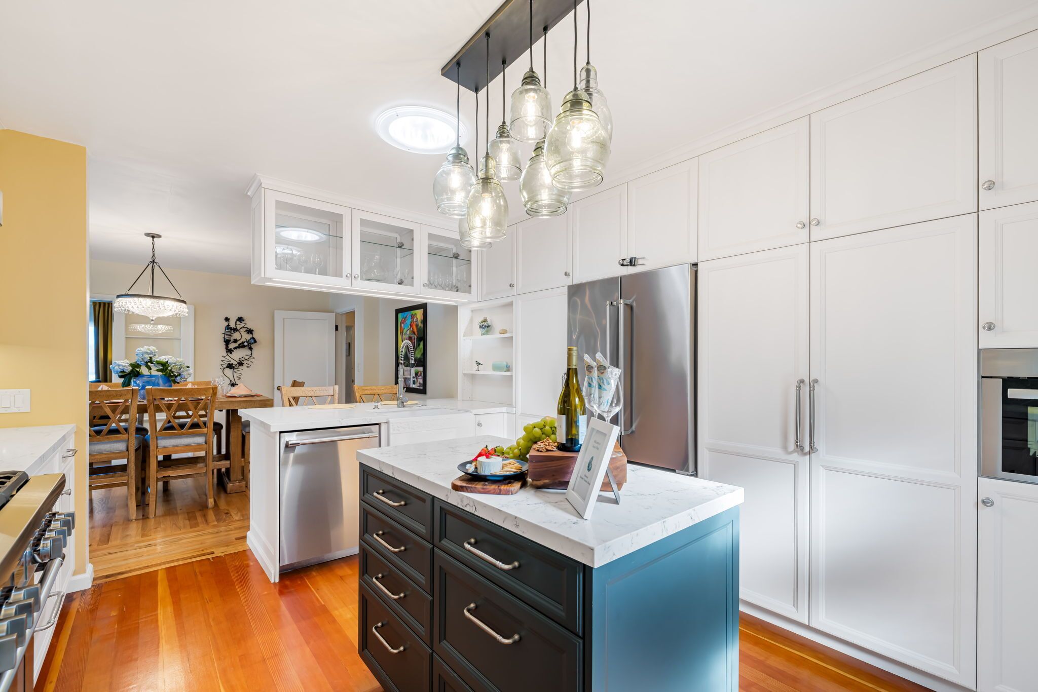 A modern kitchen with white cabinetry, a blue island, stainless steel appliances, and pendant lighting.