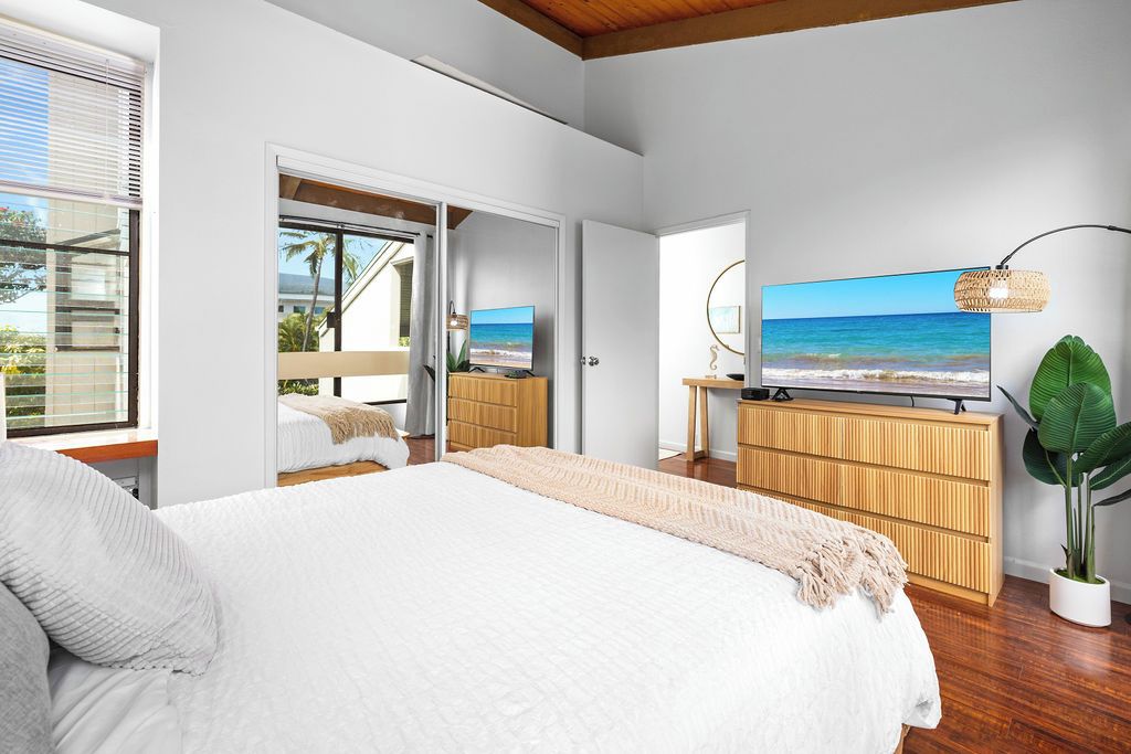 A bedroom with a large bed, a TV, and a view of the ocean.