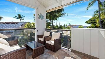 A covered outdoor seating area with wicker furniture and a glass table, overlooking a residential neighborhood with solar panels on rooftops.