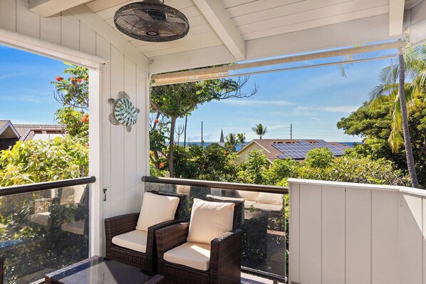 A covered balcony with wicker furniture and a view of the neighborhood.