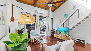 A spacious living room with a ceiling fan, a large TV, and a staircase leading to an upper level.