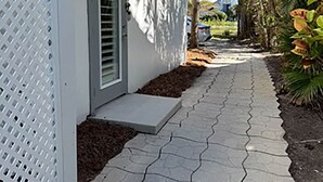 Un sendero que lleva a una casa de fachada blanca y un pequeño porche.