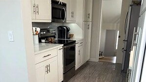 Una cocina con armarios blancos, un microondas negro, una cafetera y un horno de acero inoxidable.