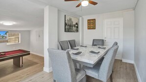 A dining area with a marble table, grey upholstered chairs, a ceiling fan, and a pool table.