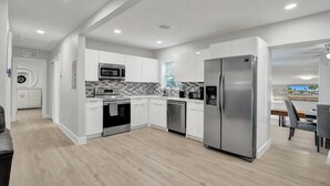 A modern kitchen with white cabinets, stainless steel appliances, and a wooden floor.
