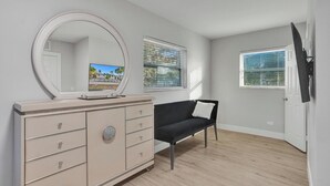 A room with a large mirror, a black sofa, a dresser, and two windows with blinds.