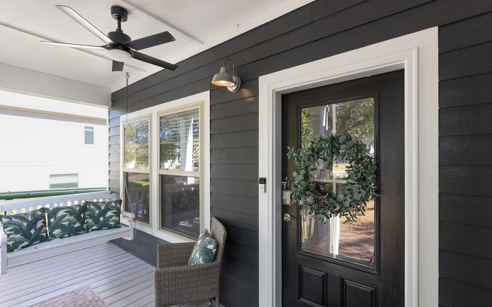 A porch with a ceiling fan, a wicker chair with a cushion, and a door with a wreath.