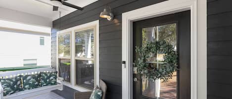 A porch with a ceiling fan, a wicker chair with a cushion, and a door with a wreath.